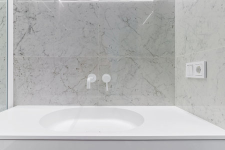 Modern bathroom with white faucets and shower, walls lined with white marble.の写真素材