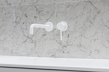 Modern bathroom with white faucets and shower, walls lined with white marble.の写真素材