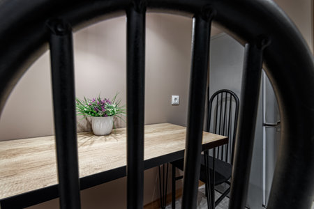 Dining table standing against the wall, with black metal chairs and a flower standing on the table, local lighting with lamps.の写真素材