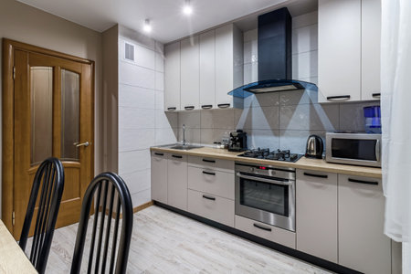 View of a modern kitchen with blue hood, kitchen appliances and dining table.の写真素材