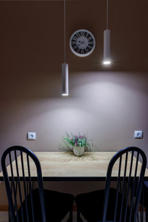 Dining table standing against the wall, with black metal chairs and a flower standing on the table, local lighting with lamps.の写真素材