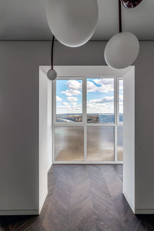 Empty apartment with large floor-to-floor window overlooking nature and blue sky with clouds.の写真素材