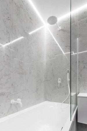 Modern bathroom with white faucets and shower, walls lined with white marble.の写真素材