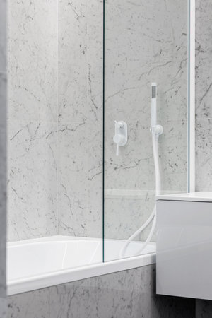 Modern bathroom with white faucets and shower, walls lined with white marble.の写真素材