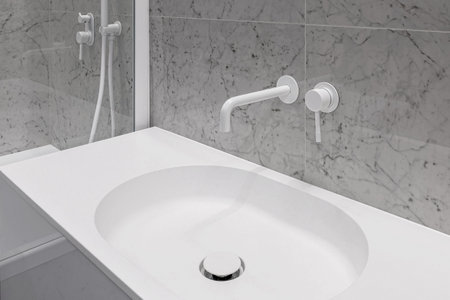 Modern bathroom with white faucets and shower, walls lined with white marble.の写真素材