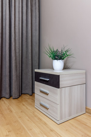 Light bedside table with a black shoe and a potted flower standing on it, against the background of the wall and curtains.の写真素材