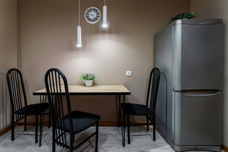 Dining table standing against the wall, with black metal chairs and a flower standing on the table, local lighting with lamps.の写真素材