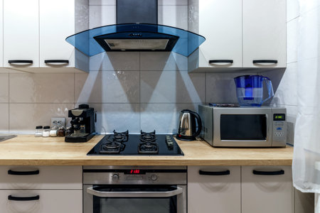 View of a modern kitchen with blue hood, kitchen appliances and dining table.の写真素材