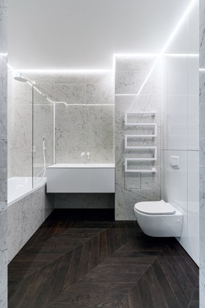 A luxurious interior in the bathroom with a bathroom, a shower on a shelf and a walk in the shower. White marble and dark brown floor. White cranes and plumbing.の写真素材