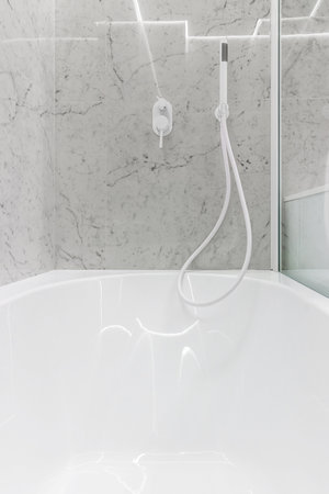 Modern bathroom with white faucets and shower, walls lined with white marble.の写真素材