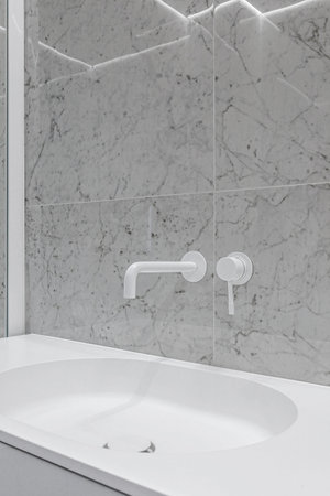 Modern bathroom with white faucets and shower, walls lined with white marble.の写真素材