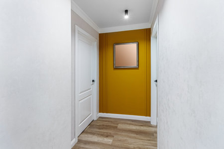 White door to the room at the end of a long corridor with a yellow wall and a painting.の写真素材