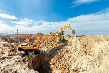 Two Excavators are digging soil in the construction site on sky background,with white fluffy cloud.の写真素材