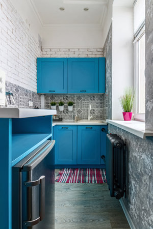 Very small kitchen with blue cabinets and window.の写真素材