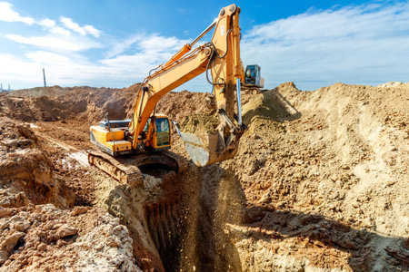 Two Excavators are digging soil in the construction site on sky background,with white fluffy cloud.の写真素材