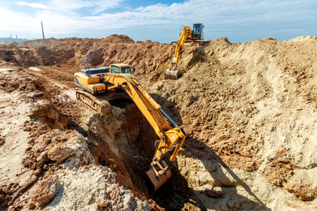 Two Excavator are digging soil in the construction site on sky background,with white fluffy cloudの写真素材