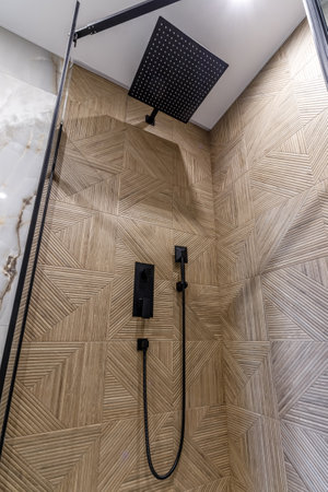 Close up of the shower area. On the wall is a black faucet with a large shower headの写真素材
