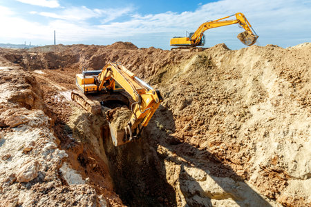 Two Excavators are digging soil in the construction site on sky background,with white fluffy cloud.の写真素材