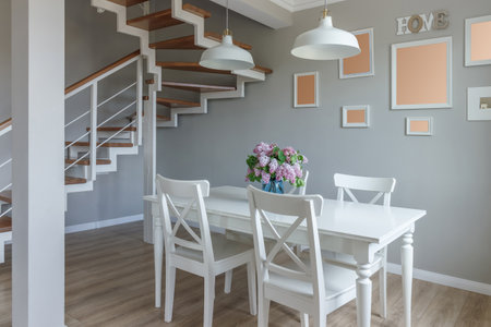 Large dining table in a modern house, with white chairs and a beautiful bouquet of lilacs in a blue vase.の写真素材