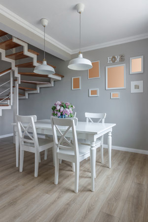 Large dining table in a modern house, with white chairs and a beautiful bouquet of lilacs in a blue vase.の写真素材
