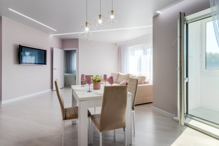A modern living room combined with a kitchen, in light colors. Dining table with pink tableware.の写真素材