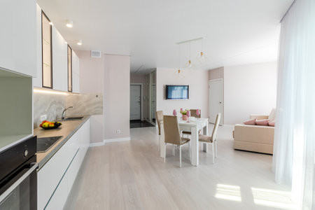 A modern living room combined with a kitchen, in light colors. Dining table with pink tableware.の写真素材