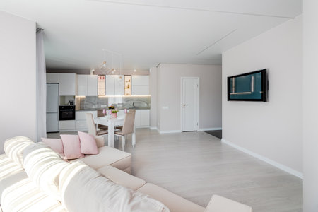 A modern living room combined with a kitchen, in light colors. Dining table with pink tableware.の写真素材