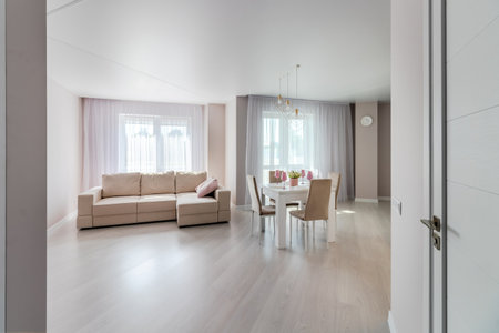 A modern living room combined with a kitchen, in light colors. Dining table with pink tableware.