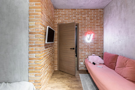 Entrance to the children's room. The walls are made of clay red bricks, a pink sofa, a white TV on the wall.の写真素材