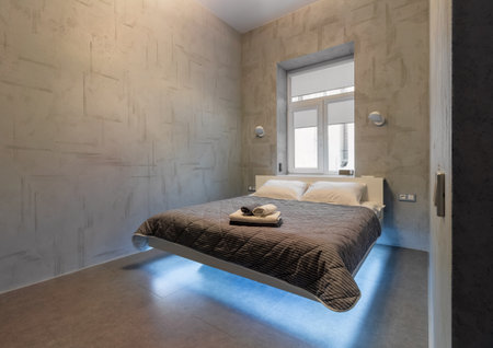 Bed in the bedroom, against the background of the window and glowing sconces on the wall.の写真素材