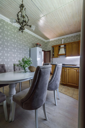 The interior of a modern light dining room with a long oval table surrounded by seats and suspended lamps and a bouquet of flowersの写真素材