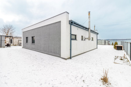 Modern one-storey house with a flat roof in winter, the plot is covered with snowの写真素材