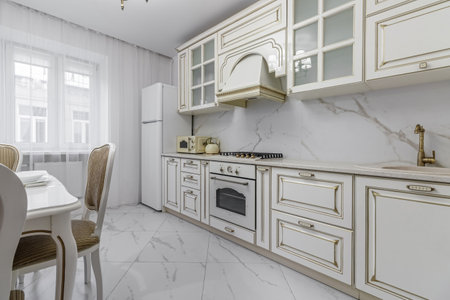 A beautiful kitchen detail with white cabinets, a gold faucet, white marble countertops, and a brown picket ceramic tile backsplash.の写真素材