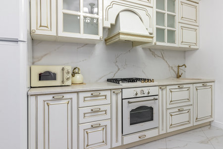 A beautiful kitchen detail with white cabinets, a gold faucet, white marble countertops, and a brown picket ceramic tile backsplash.の写真素材