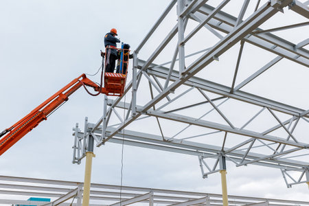 Man worker on a crane performs high-rise work on welding metal structures of new tower at height.