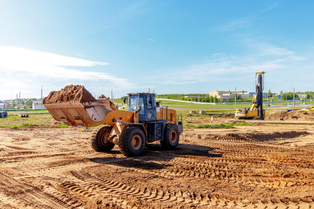 A heavy loader is moving a large amount of dirt at a construction site in an urban area on a clear dayの写真素材