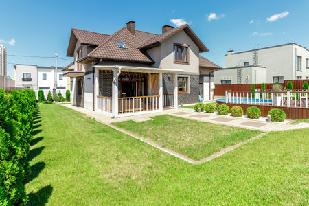 The image shows a beautifully landscaped backyard featuring an elevated pool, surrounded by greenery and a comfortable seating area.の写真素材