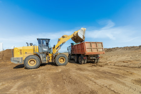 This image captures industrial heavy machinery in action, showcasing an excavator loading a truck at...