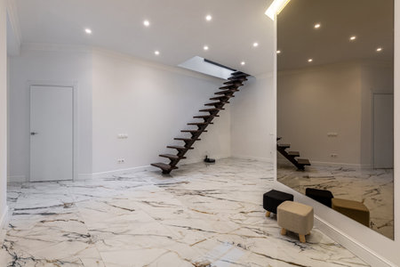 A spacious interior featuring a floating wooden staircase, marble flooring, a large mirror, and recessed ceiling lighting, creating a sleek and elegant design.の写真素材