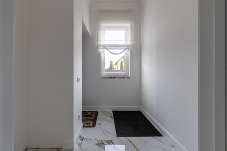 A bright and minimalist entryway featuring marble flooring, white walls, a window with sheer curtains, and a modern aesthetic.の写真素材