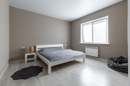 Bright minimalist bedroom with light wood flooring, white furniture, and gray bedspread creating a clean, serene atmosphere.の写真素材