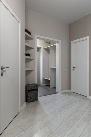 Minimalist hallway with light wood flooring, built-in shelves, white doors and view into a walk-in closet area.の写真素材
