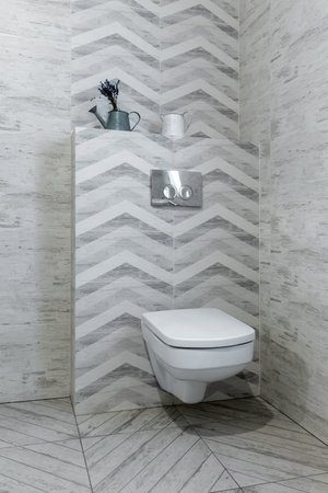 Modern wall-hung toilet with geometric gray-and-white tiles, chrome flush buttons and decorative metal pitchers on the shelf.の写真素材