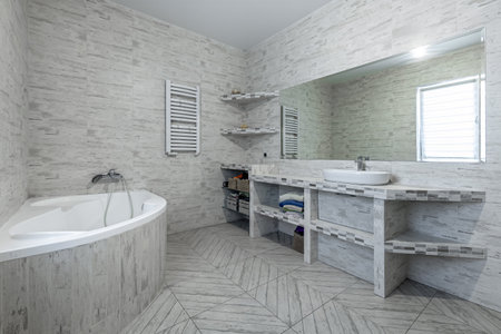 Spacious bathroom with corner bathtub, large mirror, open shelves, modern sink and bright daylight from window.の写真素材