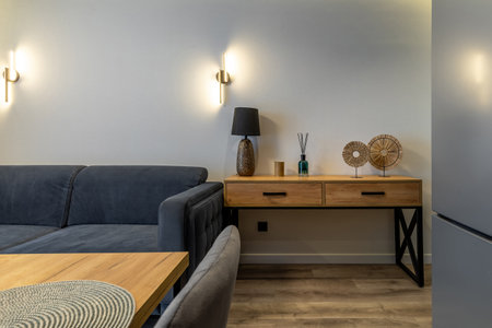 Cozy lounge area featuring a gray sofa, wooden console table with decorative accents, warm wall lights and a glimpse of the dining space.の写真素材
