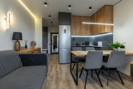 Modern kitchen and living room with wood cabinetry, soft gray chairs, dining table, cozy lighting and minimalist decor.の写真素材