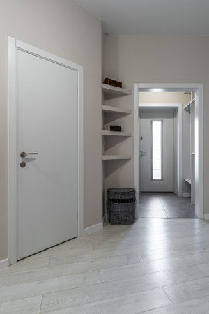 Clean modern hallway with light wood flooring, white doors, built-in corner shelves and a view into the entrance area.の写真素材