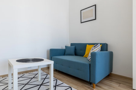 Modern light interior with blue sofa, colorful pillows, white table and rug in a cozy minimalist living space.の写真素材