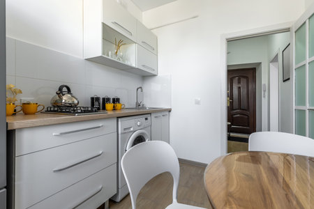 Bright compact kitchen with wooden countertop, gas stove, white cabinets, black containers, yellow mugs and modern decor.の写真素材