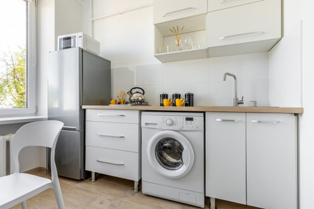 Functional kitchen interior with washing machine, sink, kettle, mugs, modern appliances and wooden countertop in a bright home.の写真素材